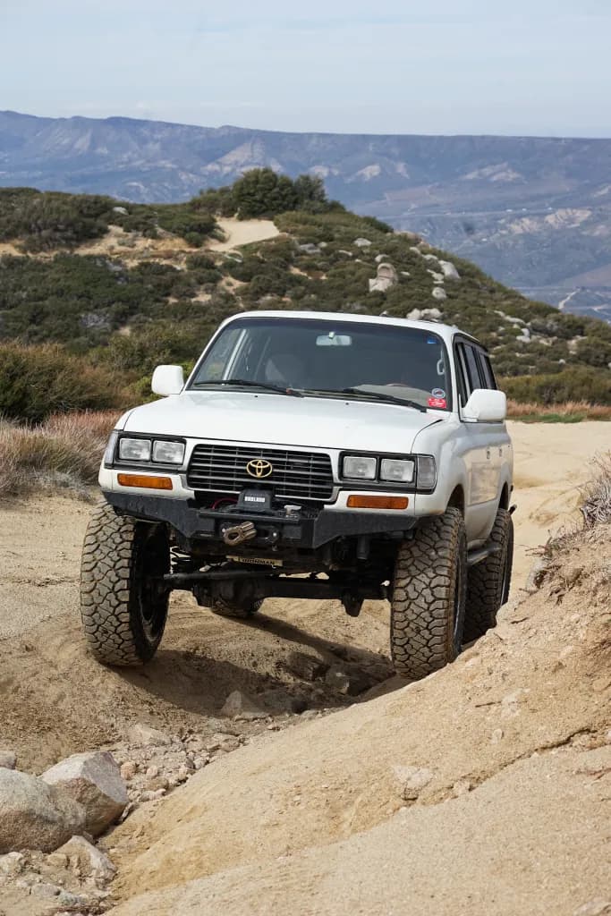 Toyota Land Cruiser FZJ80 climbing a sandy dune with mountains in the background